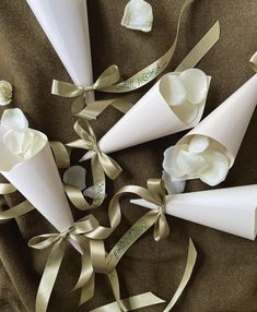 three white cones with ribbons and flowers in them on a brown cloth covered tablecloth