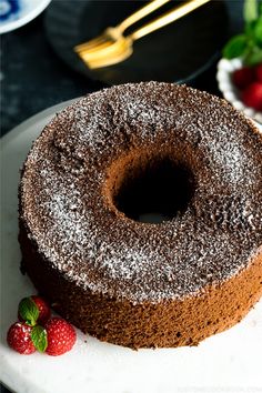 a chocolate cake sitting on top of a white plate with strawberries next to it