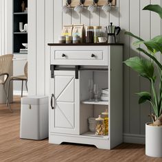 a kitchen with white cabinets and wood flooring next to a green potted plant