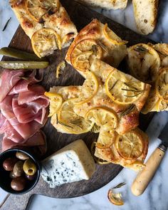 an assortment of meats and cheeses on a wooden platter with olives