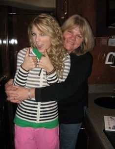 two women standing in a kitchen hugging each other and giving the peace sign with their fingers