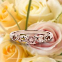 a pink diamond ring sitting on top of some white and yellow flowers with roses in the background