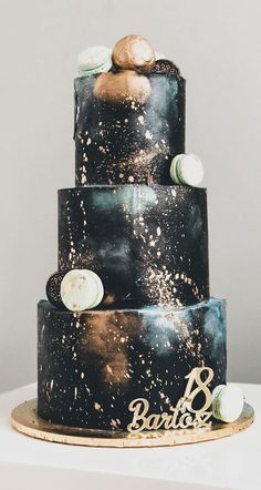 a three tiered black cake with gold and white decorations on it's side