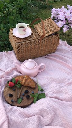 a wicker basket and tea set on a blanket in front of purple flowers with strawberries