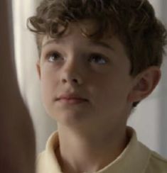 a young boy with curly hair is looking at himself in the mirror while he's wearing a yellow shirt