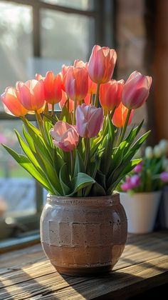 a vase filled with lots of pink flowers on top of a wooden table next to a window