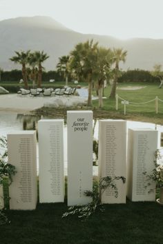 several white plaques with names on them sitting in the grass next to some water and palm trees