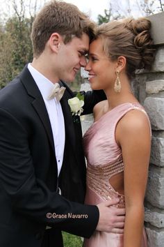 a man and woman in formal wear standing next to each other near a stone wall