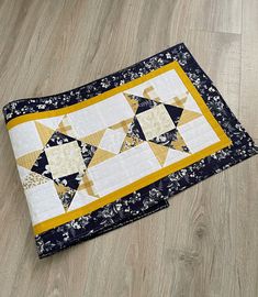 a yellow and black quilted placemat on the floor with wood floors in the background