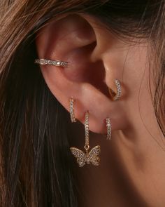 a close up of a person's ear wearing gold and diamond butterfly hoop earrings