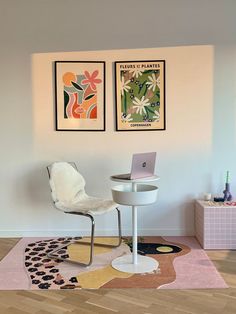 two paintings hang on the wall next to a white chair and table with a laptop