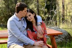 a man and woman sitting on a bench in the grass with their arms around each other