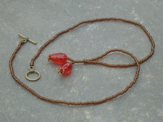 a red glass beaded necklace on a brown cord with a gold clasp and hook