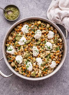 a pan filled with pasta and vegetables next to a bowl of pesto sauce on the side