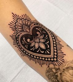 a black and white heart tattoo on the left arm, with an intricate design in the middle