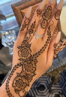 a woman's hand with henna tattoos on it and her nails in the shape of flowers