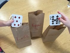 three bags with playing cards on them sitting on a table next to two people's hands