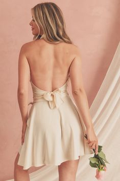 the back of a woman in a short white dress holding a rose and looking down