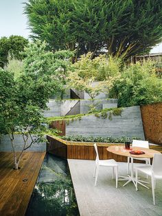 an outdoor dining area with table and chairs next to the water feature, surrounded by greenery