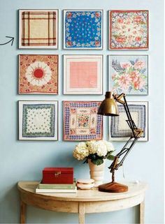 a table with a lamp and some pictures on the wall above it, along with flowers