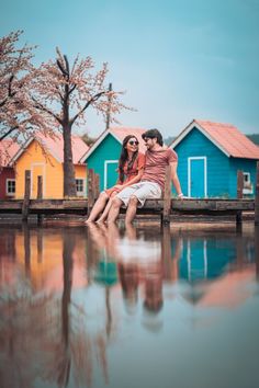 two people are sitting on a bench near the water and colorful houses in the background