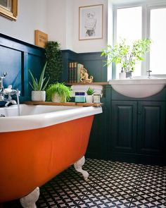 an orange bath tub sitting in a bathroom next to a sink and window with potted plants on it