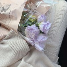 purple flowers wrapped in cellophane on top of a white knitted blanket and sweater