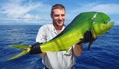 a man holding a large green fish in his hands while standing on a boat near the ocean