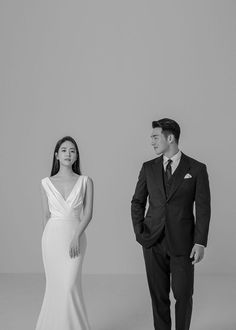 a man and woman standing next to each other in front of a white wall wearing suits