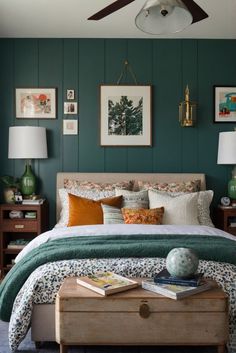 a bedroom with green walls and pictures on the wall above the bed, along with an ottoman