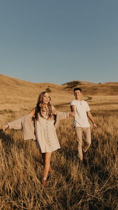 a man and woman are walking through the tall grass with their hands in the air