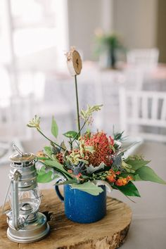 a blue mug filled with flowers sitting on top of a wooden table next to a coffee pot