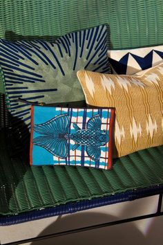 three pillows sitting on top of a green couch next to a pillow with blue and yellow designs