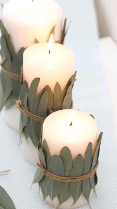 three white candles with green leaves and twine around them on a blue table cloth