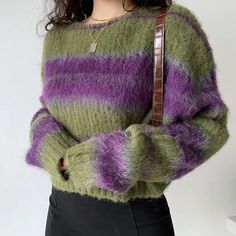 a woman wearing a green, purple and black striped sweater holding a brown leather handbag