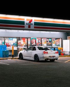 a white car is parked in front of a gas station at night with the lights on