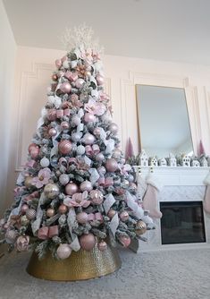 a decorated christmas tree with pink and silver ornaments in a living room next to a fireplace