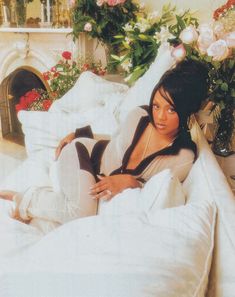 a woman laying on top of a white bed covered in blankets and pillows next to a fireplace