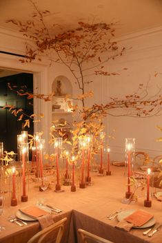 a dining table with candles and flowers in vases on the top, along with other place settings