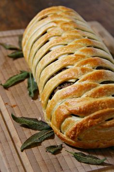 a loaf of bread sitting on top of a wooden cutting board next to sage leaves