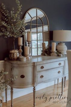 a white dresser sitting next to a mirror on top of a wooden floor covered in furniture