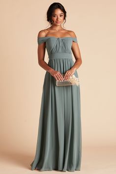 a woman in a long green dress holding a clutch and posing for the camera with her hands on her hips