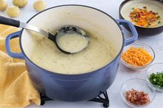 a blue pot filled with soup next to bowls of vegetables and other food on a table