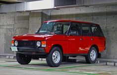 an old red station wagon is parked in a parking garage next to a concrete wall