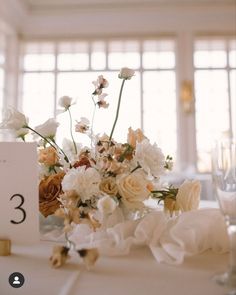 an arrangement of flowers on a table at a wedding reception in front of large windows