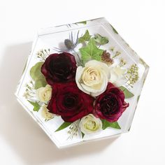 an arrangement of flowers is displayed in a glass vase on a white surface with greenery