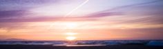 the sun is setting over the ocean with waves crashing in front of it and an airplane flying overhead