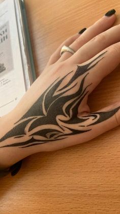 a woman's hand with a black and white tattoo design on it, next to an open book