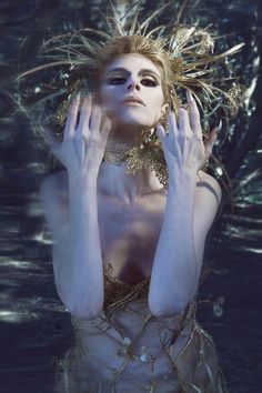 a woman with her hands on her face in the water wearing gold jewelry and chains