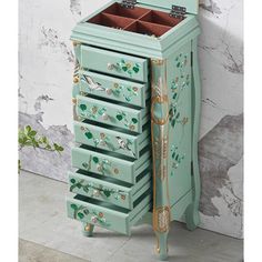 an ornately painted jewelry cabinet with drawers on the front and bottom, sits against a wall